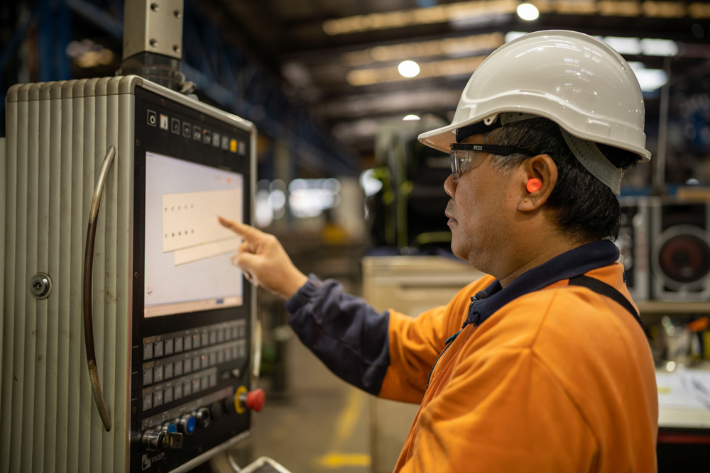photo of a main in a hard hate working in a steel fabrication factory using a touch screen computer