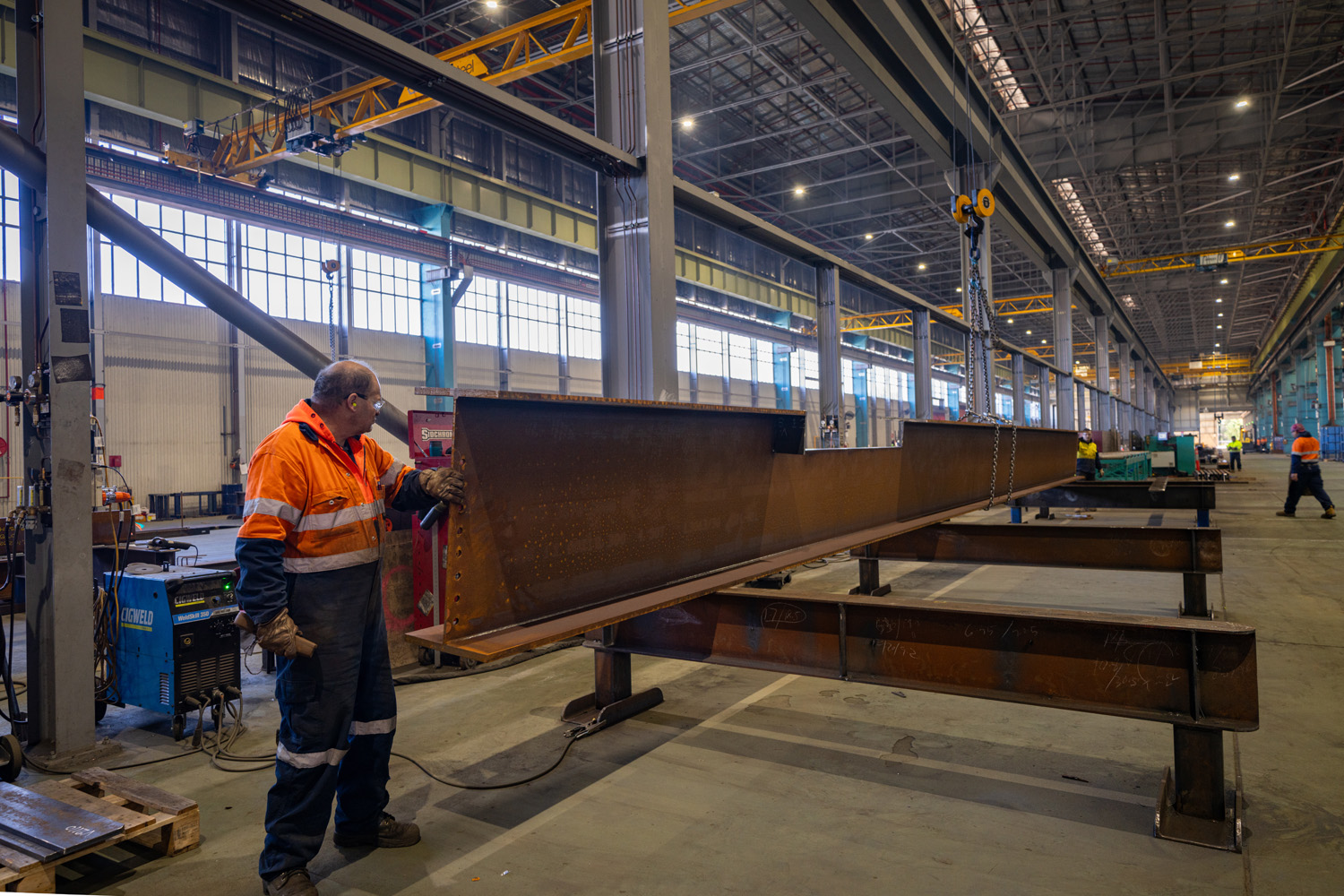 photo of men in a steel fabrication warehouse working on a very long piece of steel 